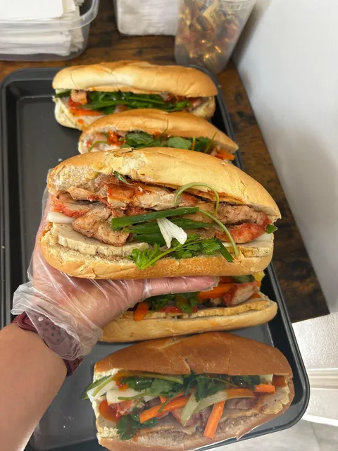 A filled bánh mì held above a tray of prepared sandwiches
