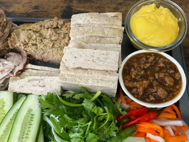 Bánh mì ingredients arranged together: sliced fillings, cucumber, cilantro, pickled vegetables, and sauces