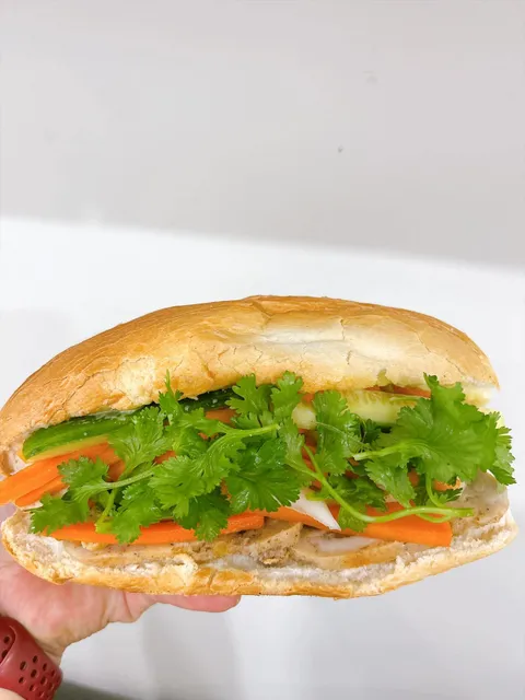 A bánh mì held up to show its fresh herbs, cucumber, and pickled vegetables