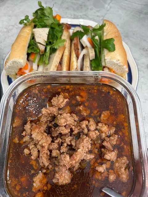 A dish of savoury filling with sliced bánh mì on a plate behind it