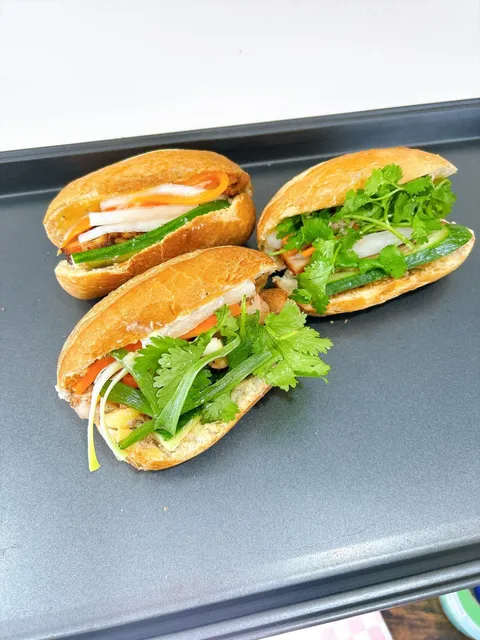 Three golden bánh mì filled with fresh herbs, cucumber, and pickled vegetables on a tray