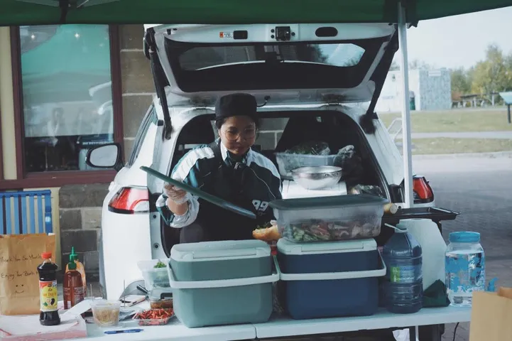 Preparing food at an outdoor stall, with ingredients and containers arranged on the table